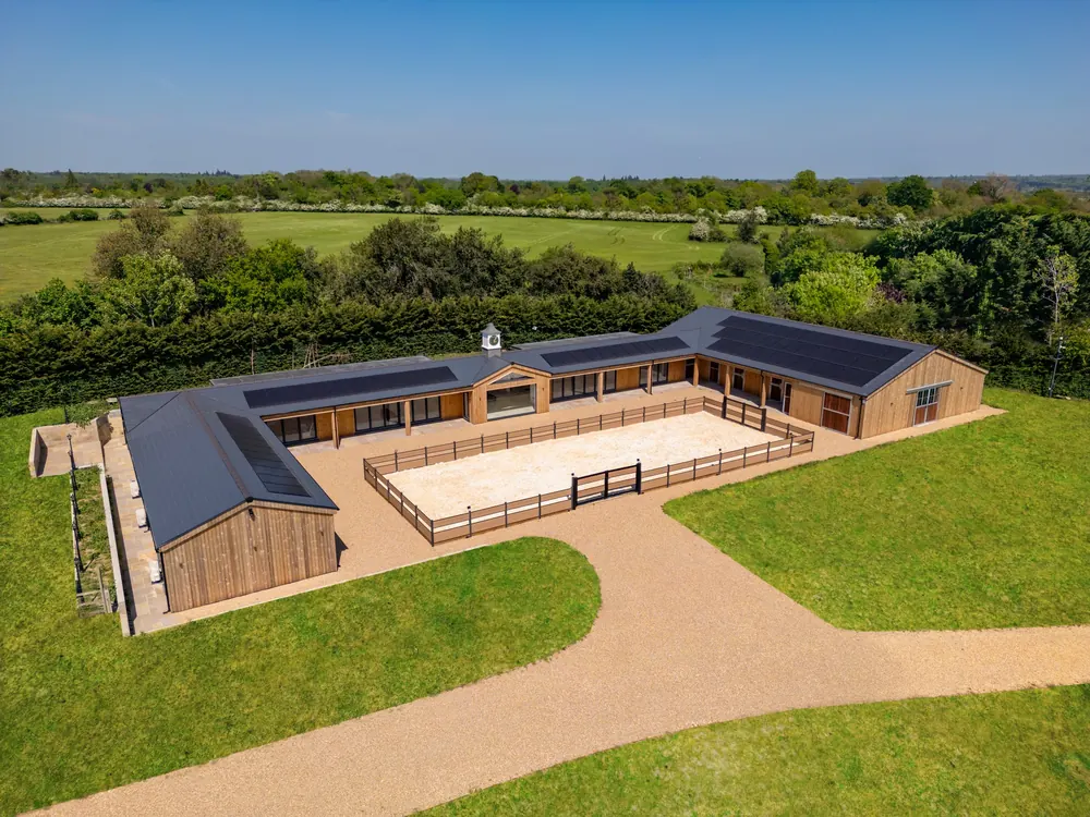Aerial view of a large bespoke Crown timber building with dark roofs, arranged around a central courtyard in open countryside
