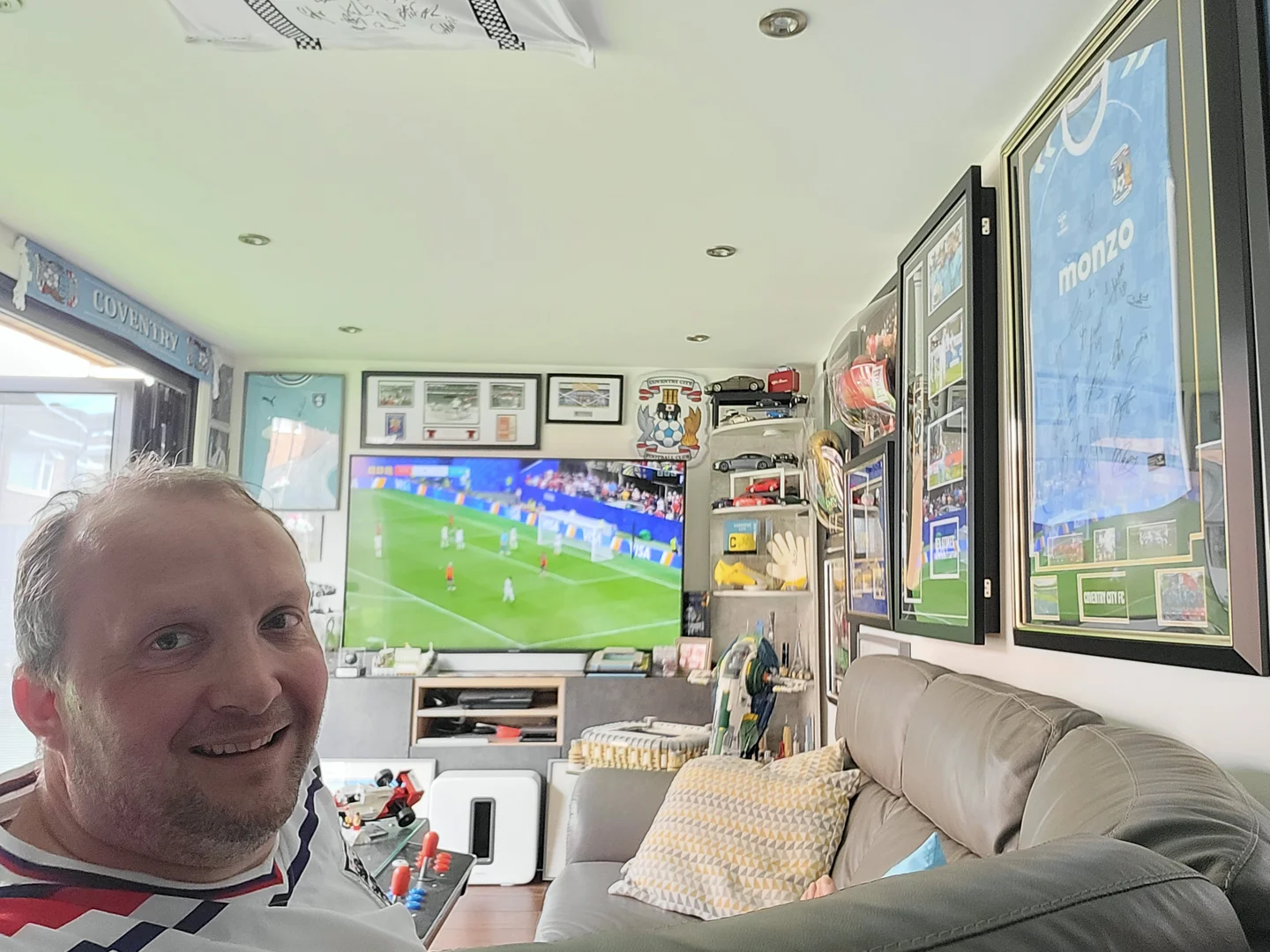 Kevin Burdett watching the World Cup on the 65-inch TV in his Crown Pavilions Clarence garden room, surrounded by framed football memorabilia