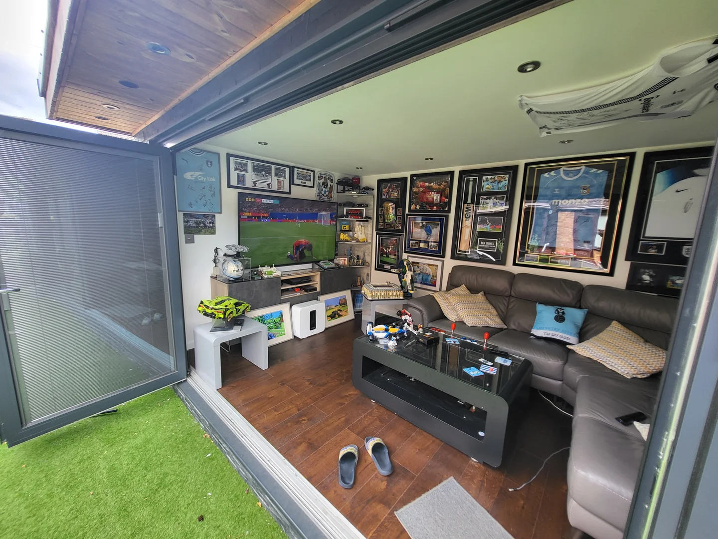 Kevin's Crown Pavilions Clarence garden room with the bi-fold doors open, showing the TV, leather sofas and memorabilia-lined walls
